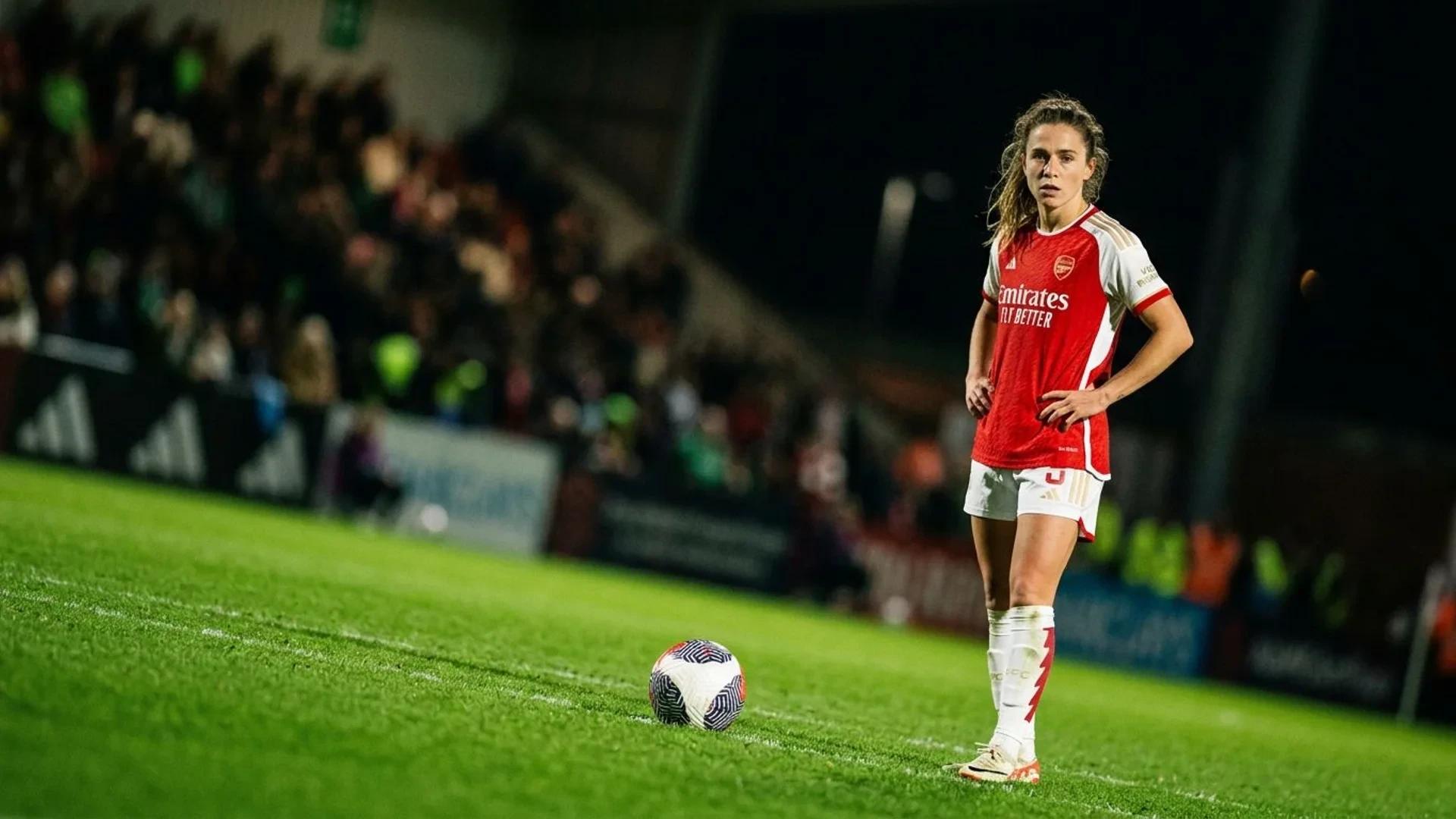 Ona Batlle in an Arsenal jersey standing on a football pitch, illuminated by a spotlight.