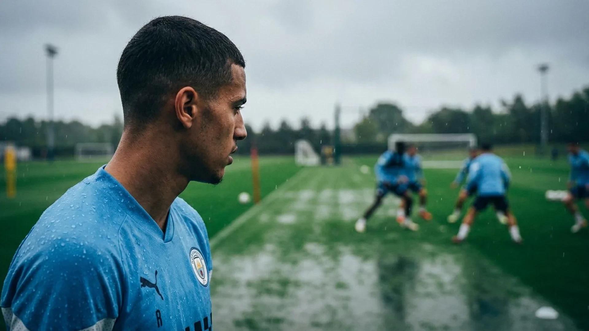 En ung Manchester City-spiller står på en regntung treningplass, med blikket fokusert fremover.