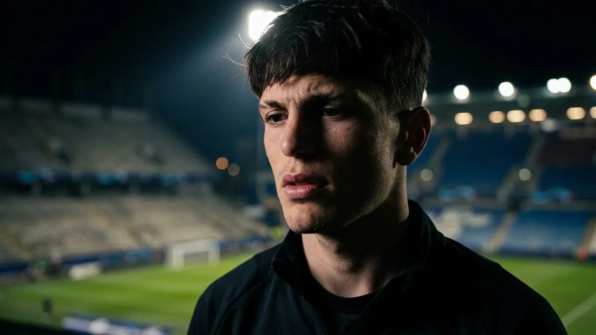 Close-up of a man reflecting in a dimly lit stadium environment.