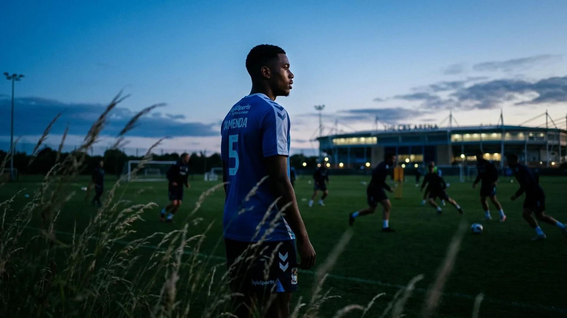 Aurèle Amenda standing on a training ground, viewed over-the-shoulder at dusk.