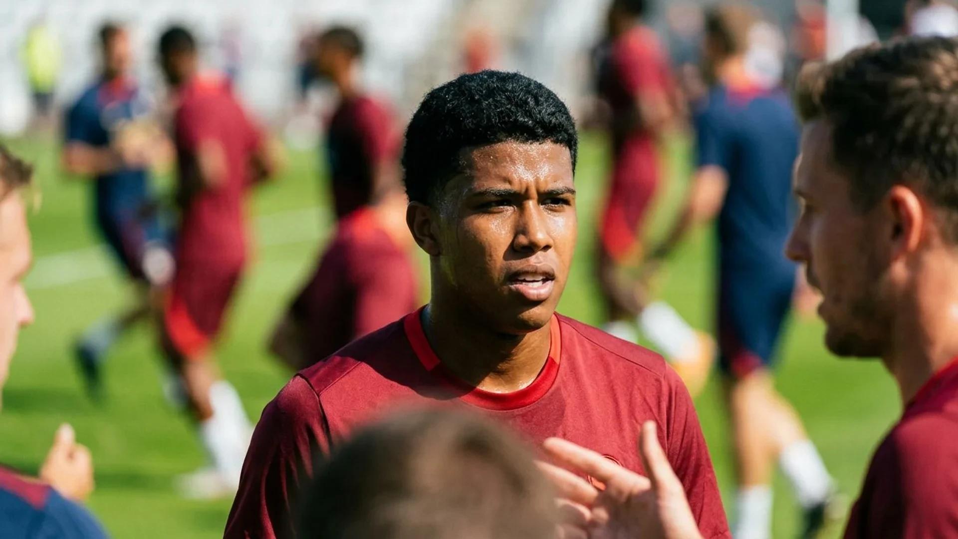 A close-up of Andrey Santos sweating during a training session in bright sunlight, with blurred teammates in the background.