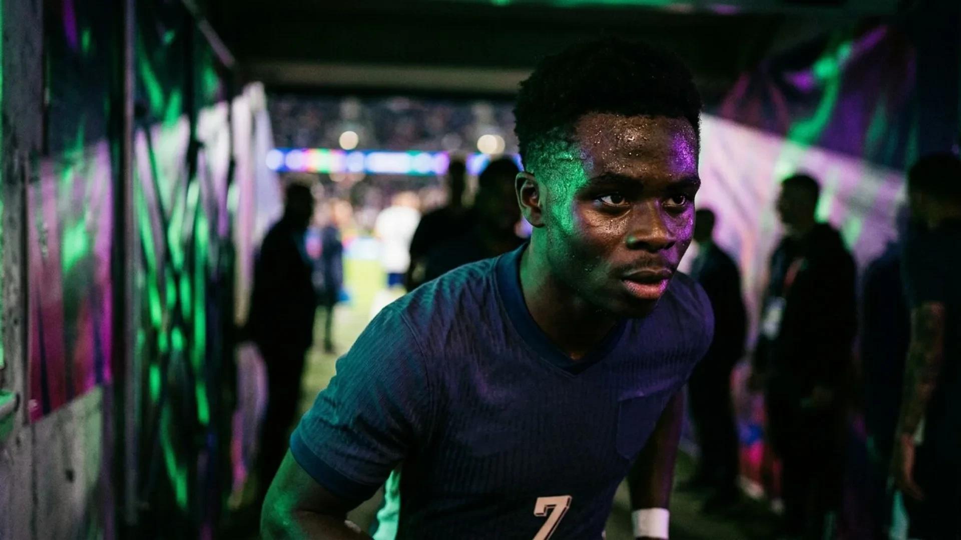 Close-up of a focused Bukayo Saka in a neon-lit tunnel, preparing for a match.