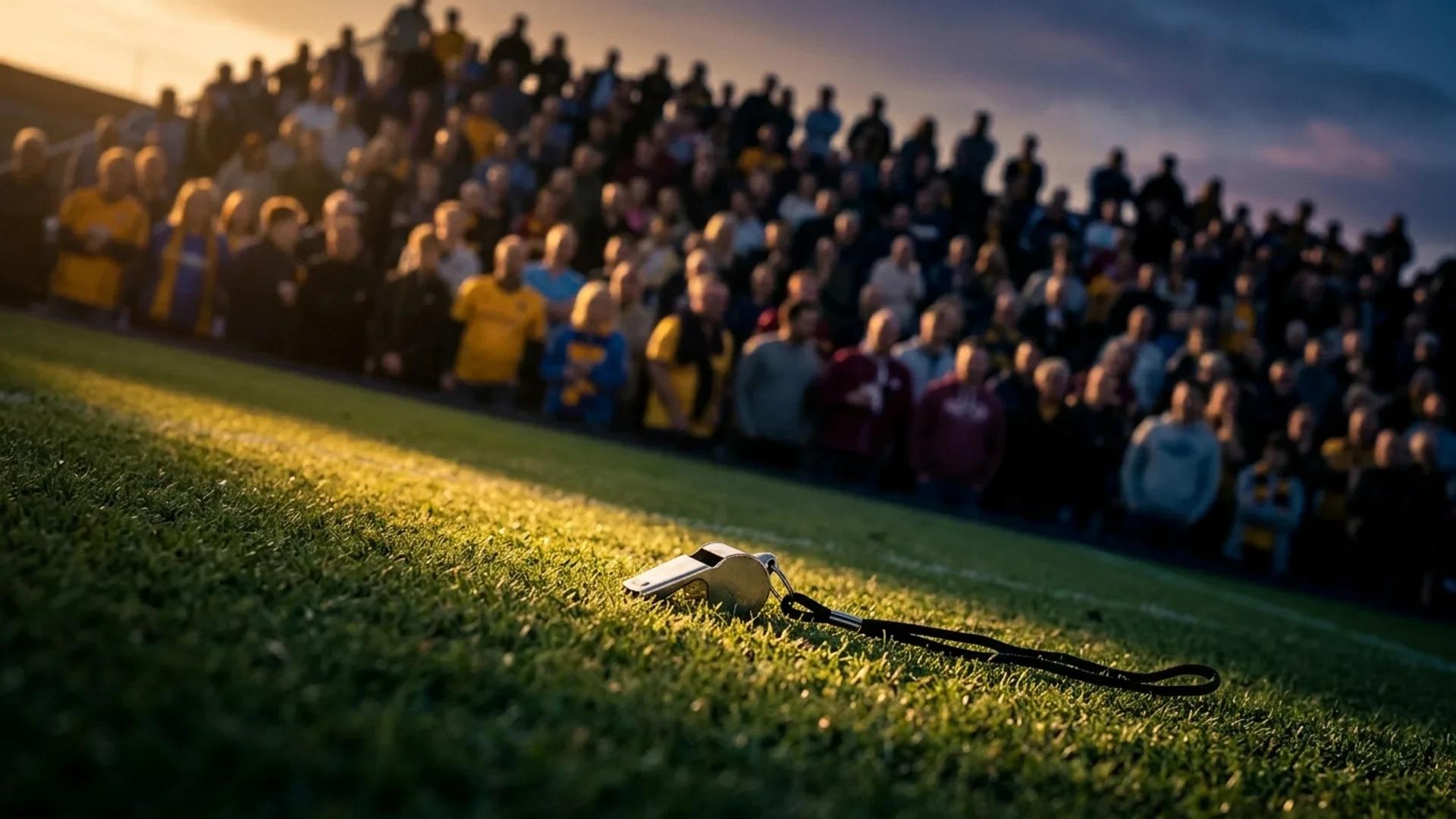 A close-up of a referee's whistle on an empty football pitch during sunset.