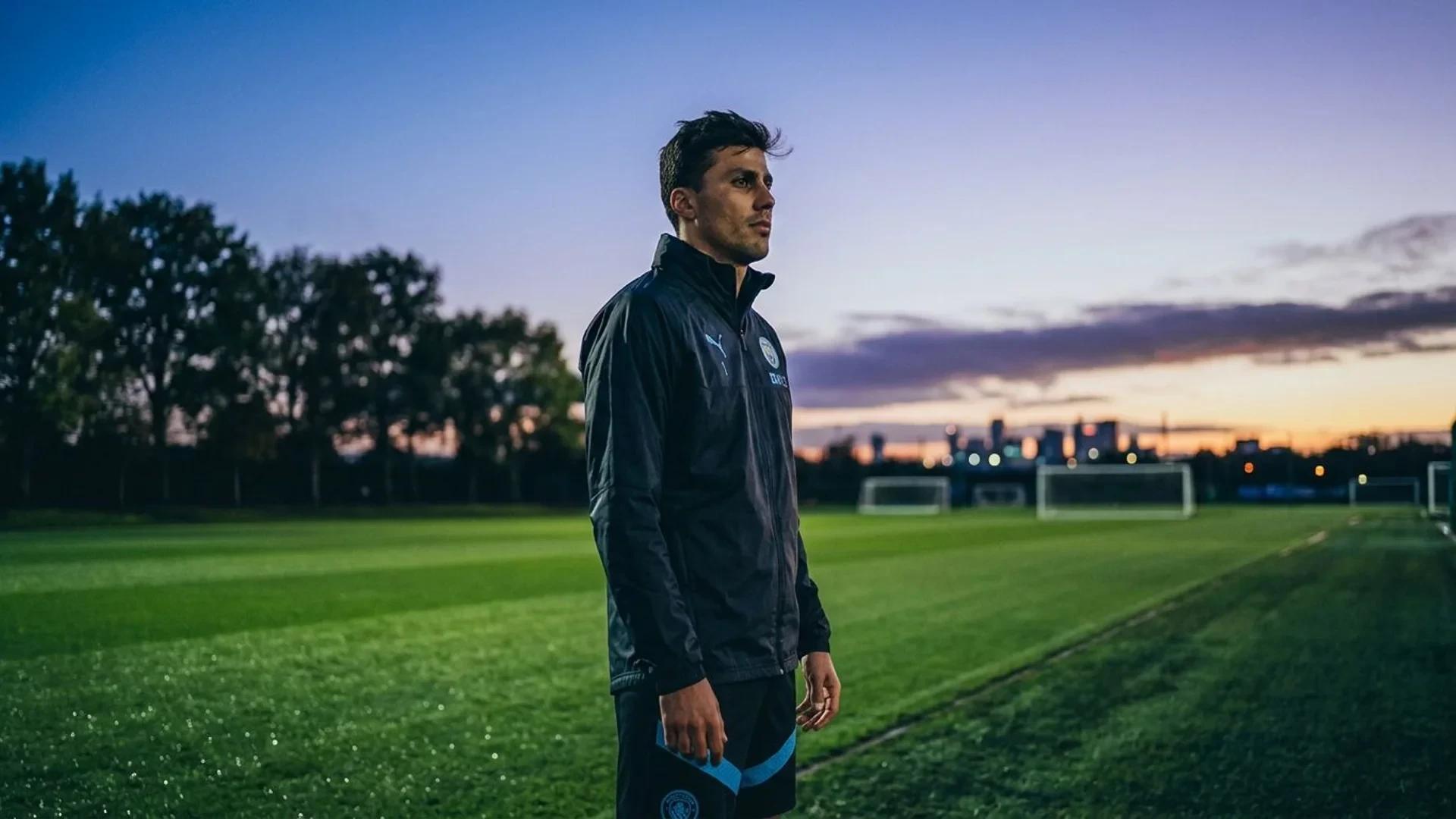 En spansk fotballspiller står alene på treningsfeltet i blåskumring og ser ettertenksomt mot horisonten.