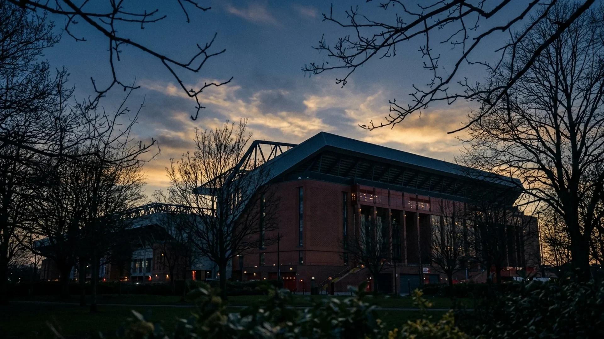 A low-angle view of Anfield stadium at dusk, framed by silhouetted trees.