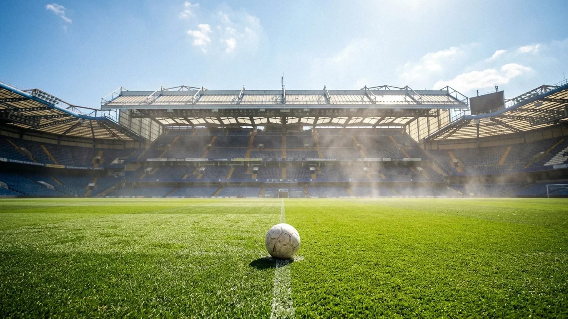 An expansive view of Stamford Bridge stadium under bright sunlight, focusing on a single football at the center of the pitch.