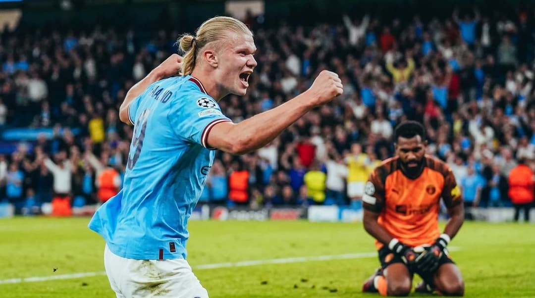 Erling Haaland celebrating in a football match with a relieved Vozinha in the background.