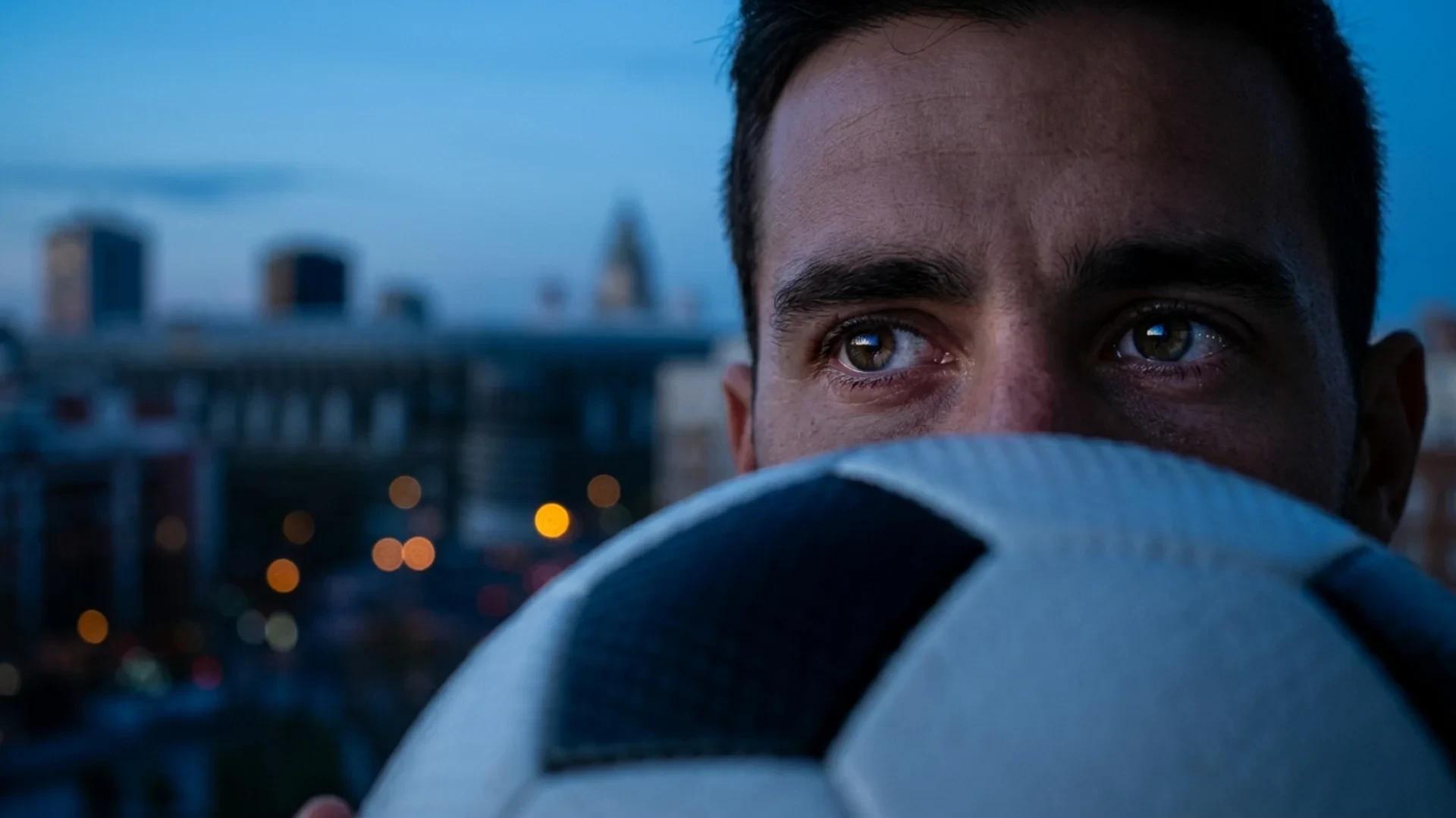 Close-up of an intense gaze reflecting dusk colors, with a soccer ball partially obscuring the view.