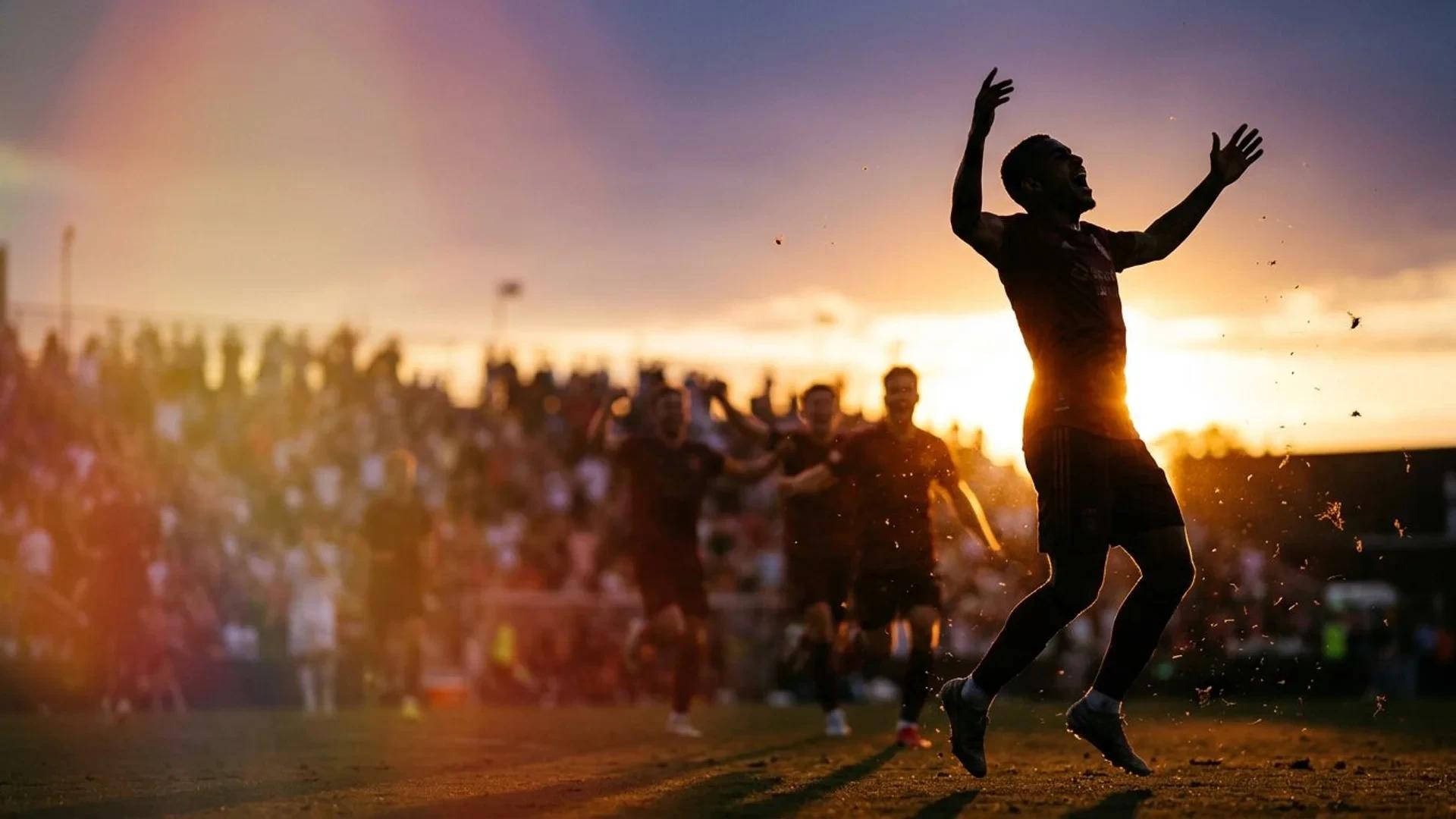 Silhouette of a football player celebrating a goal during sunset.