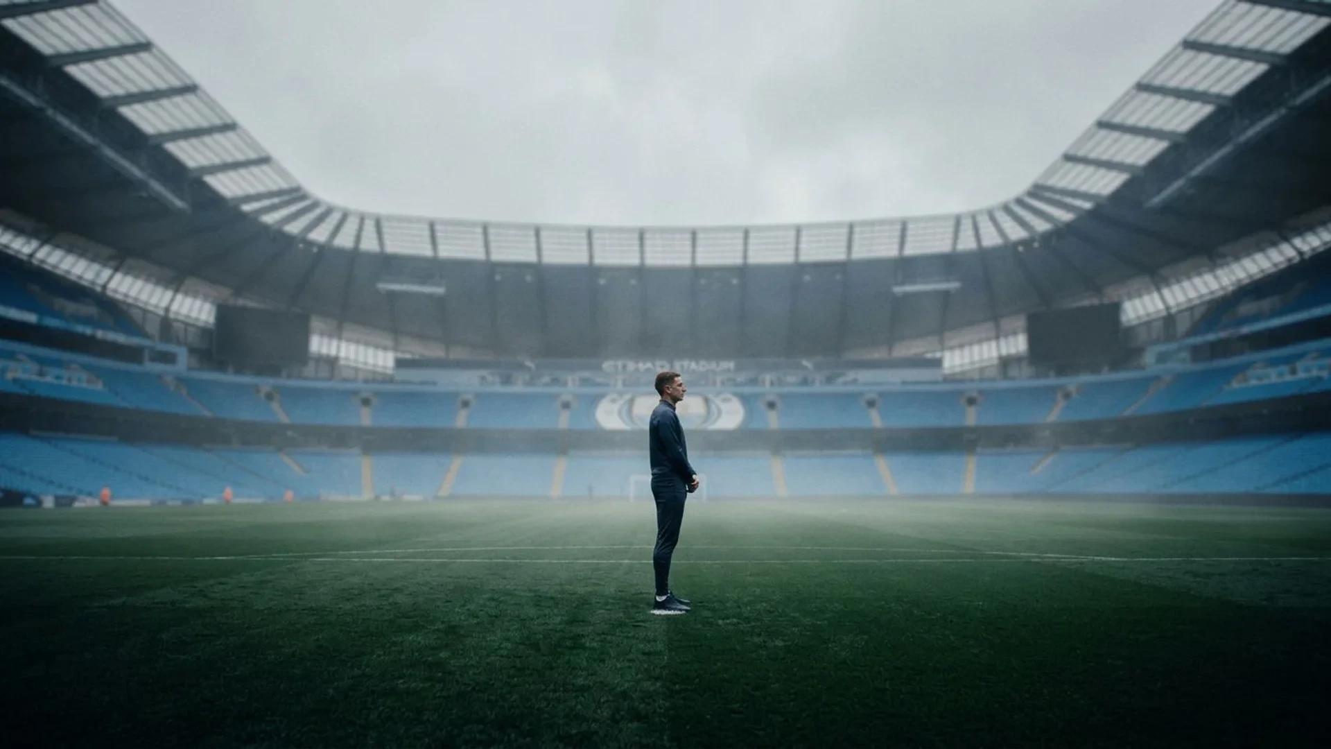 Elliot Anderson stands alone on the pitch of Manchester City's stadium, surrounded by empty seats under a gray sky.