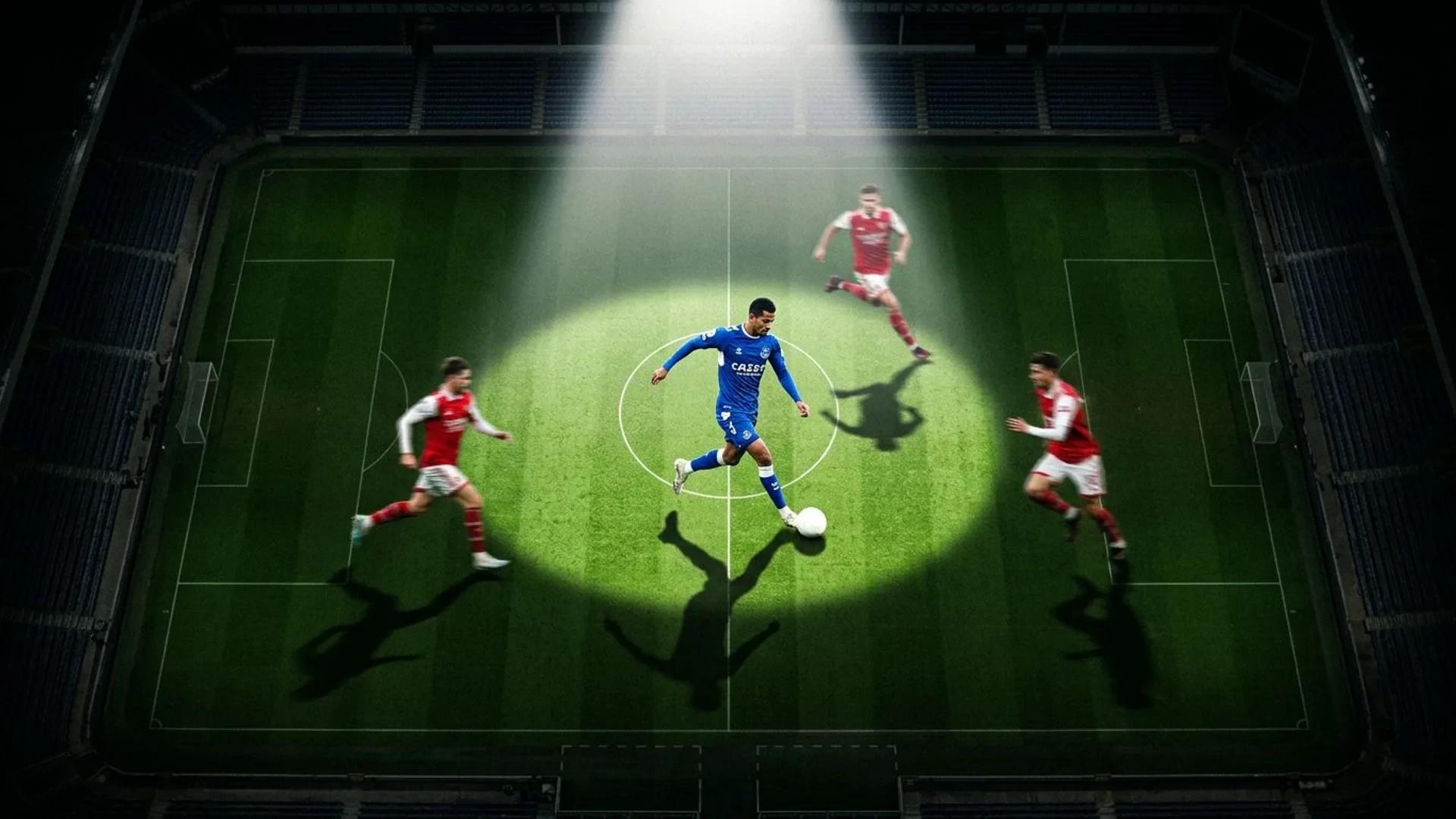 Aerial view of a soccer player in action on a green field under a spotlight.
