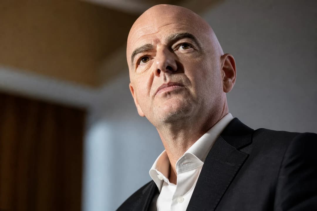 FIFA-president Gianni Infantino i nærbilde med alvorlig og bestemt ansiktsuttrykk, belyst av dramatisk kontrast-lys mot blurred institusjonsbakgrunn.