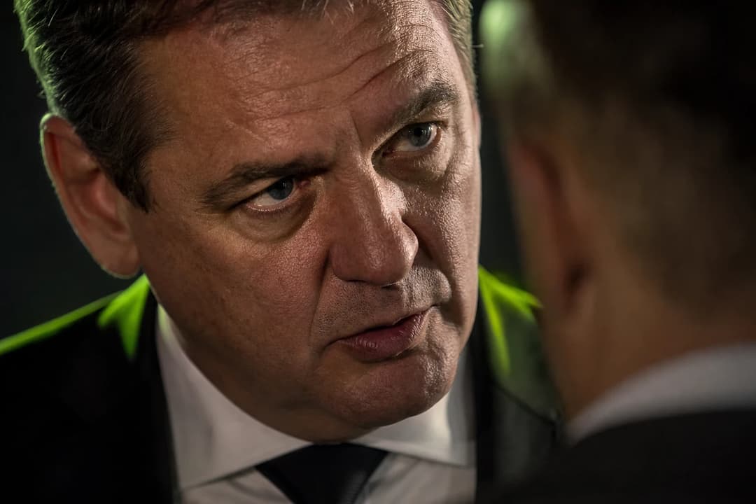 Close-up of a man with a serious expression, engaged in a conversation, illuminated by dramatic lighting.