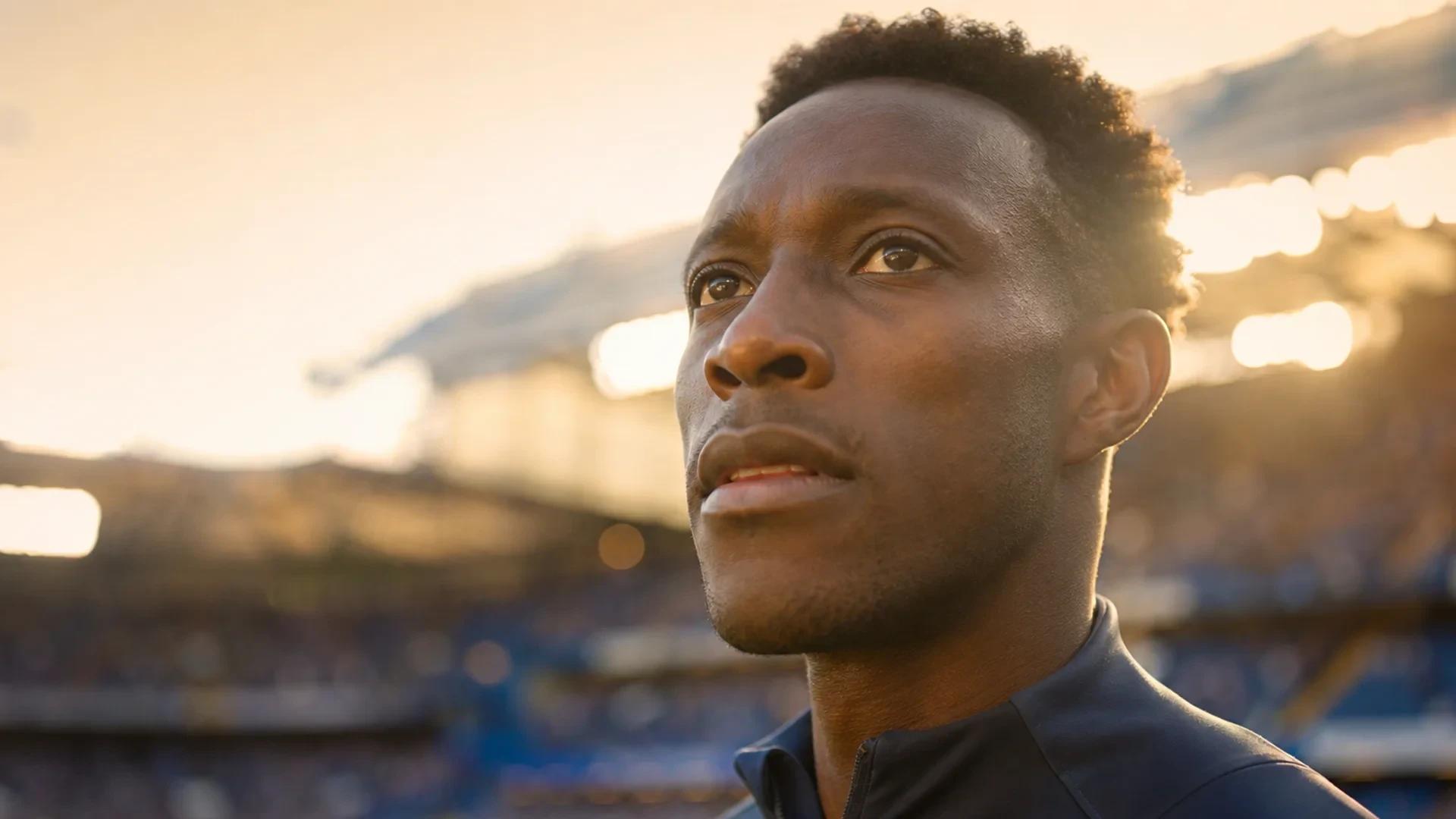 Danny Welbeck in a close-up shot, smiling with anticipation at the Stamford Bridge pitch during golden hour.