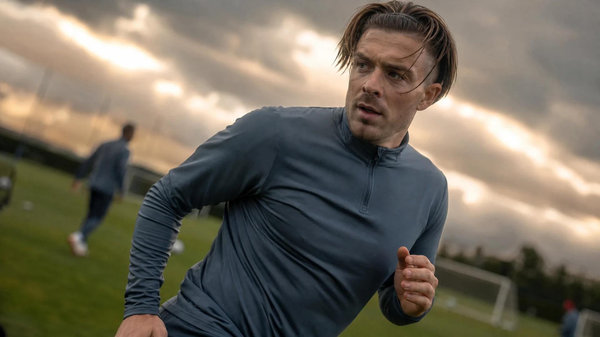Jack Grealish training alone on a soccer pitch, displaying determination amidst storm clouds.