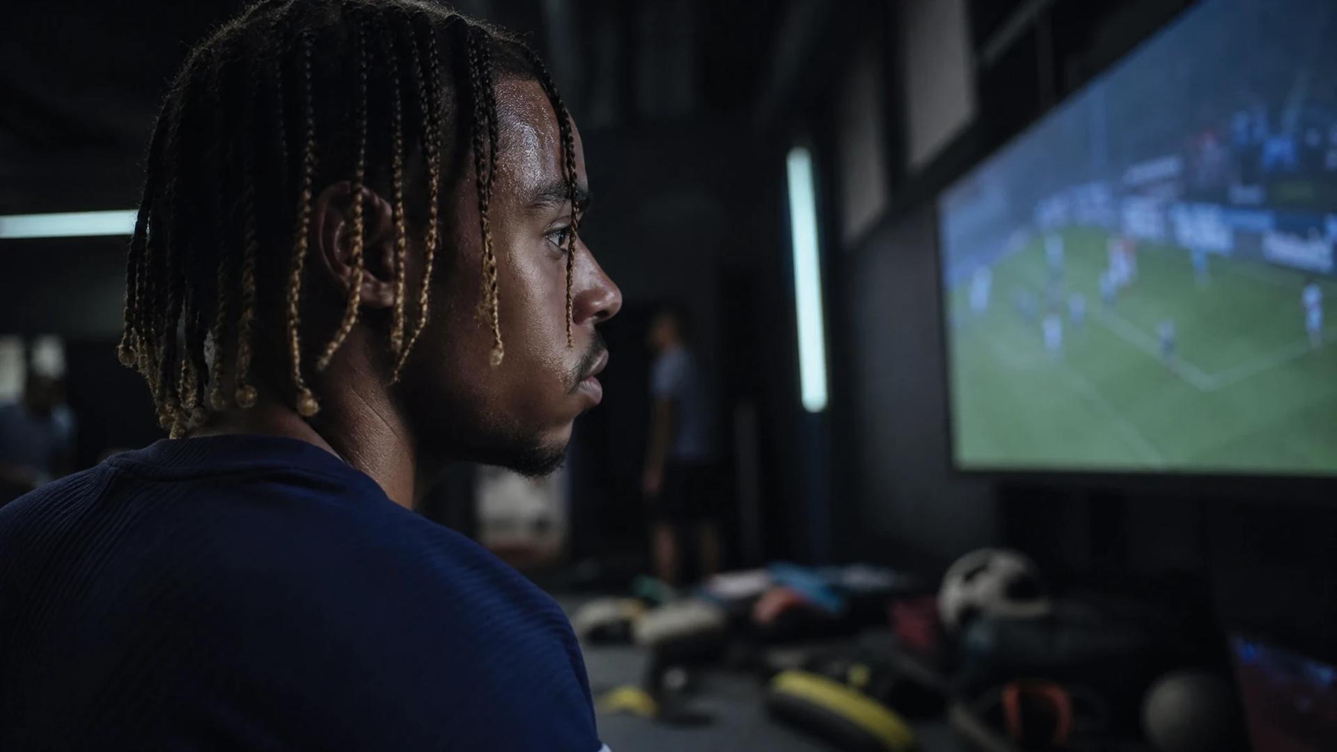 Bradley Barcola watches performance footage in a dim training room.