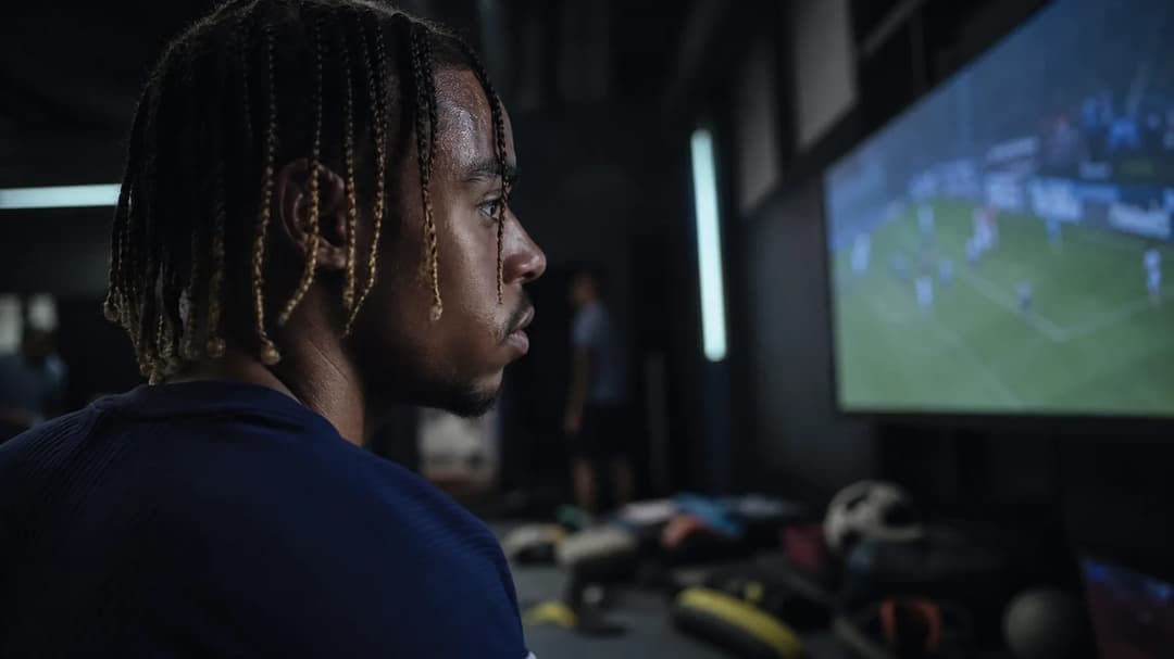 Bradley Barcola watches performance footage in a dim training room.