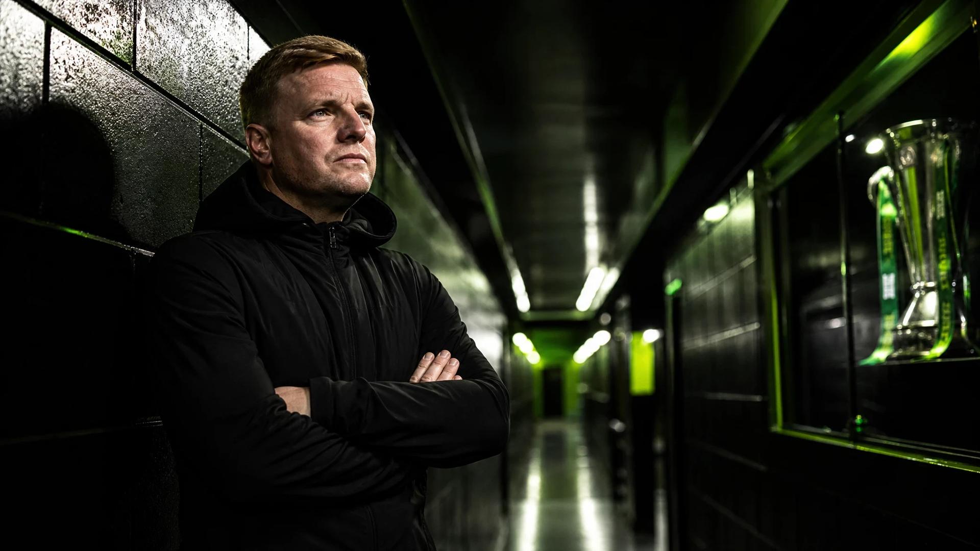 Eddie Howe stands thoughtfully in a dim corridor of St James' Park, with shadows accentuating his expression.