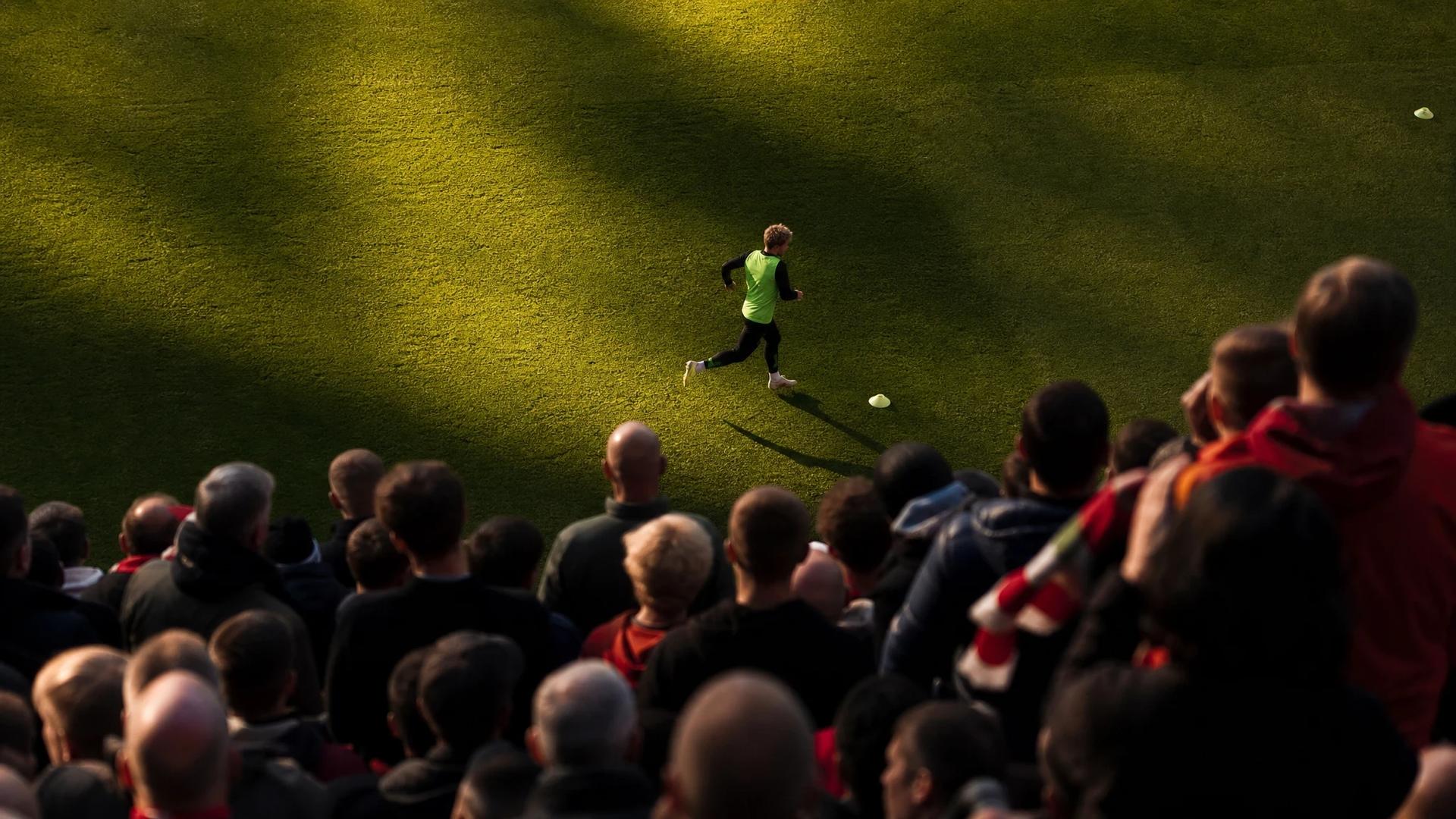 Bird's-eye view of Harvey Elliott warming up at Anfield, surrounded by a crowd of fans.