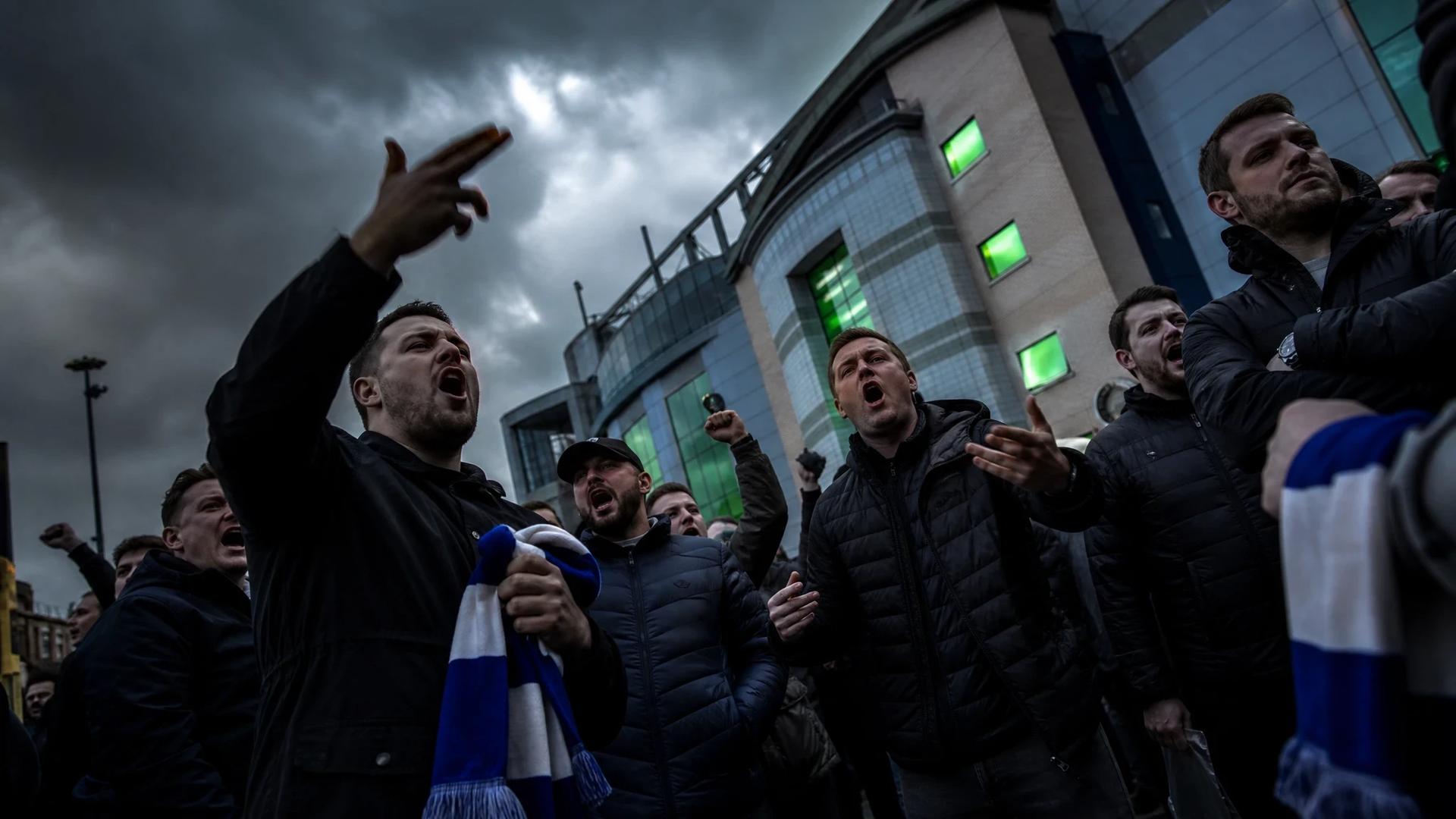 A group of Chelsea supporters outside Stamford Bridge displaying various emotions.
