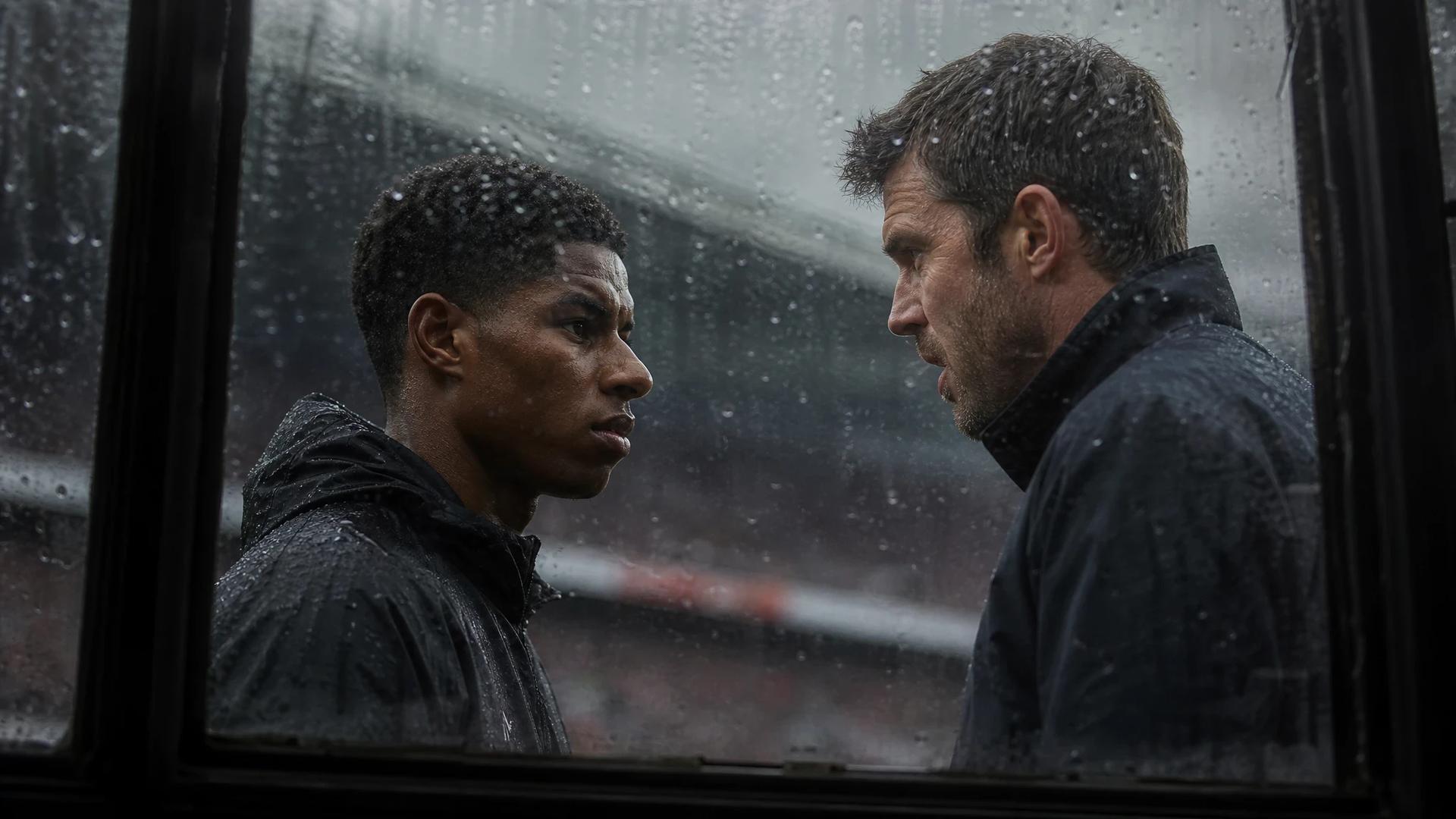 Marcus Rashford and Michael Carrick interact through a rain-soaked window at Old Trafford.