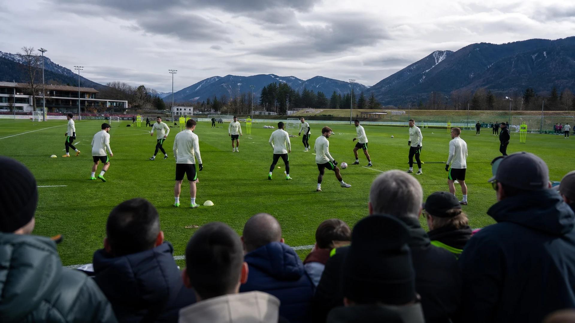 A packed training camp scene with players practicing and a crowd of fans in the foreground.