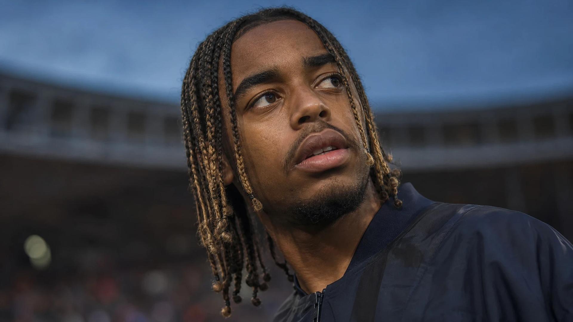 Bradley Barcola in a close-up at sunset, showing intense emotion amid a blurred stadium background.