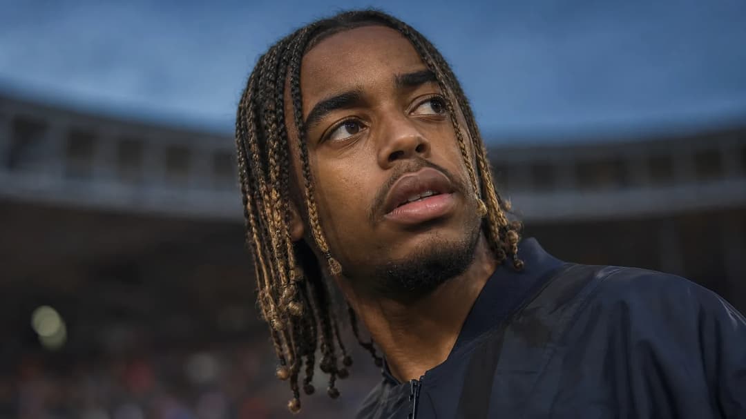 Bradley Barcola in a close-up at sunset, showing intense emotion amid a blurred stadium background.