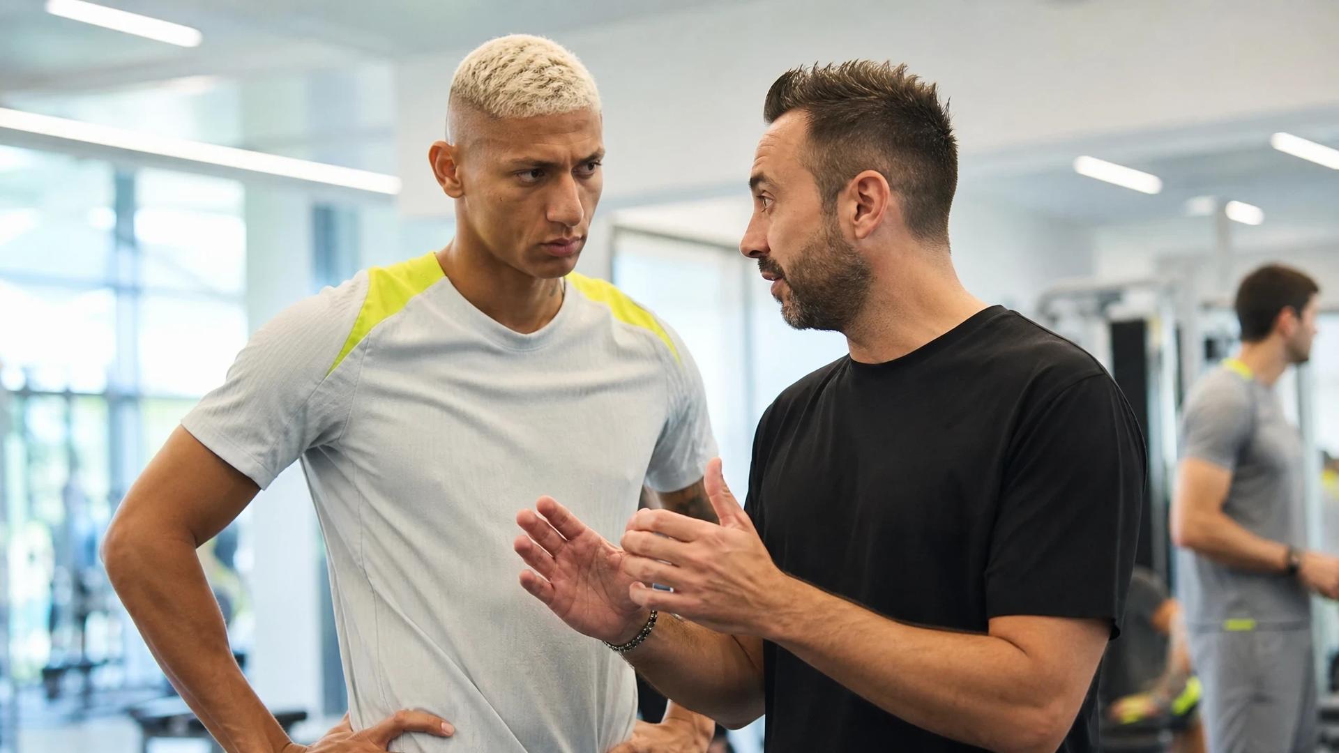 Richarlison discussing tactics with his coach in a bright training facility.
