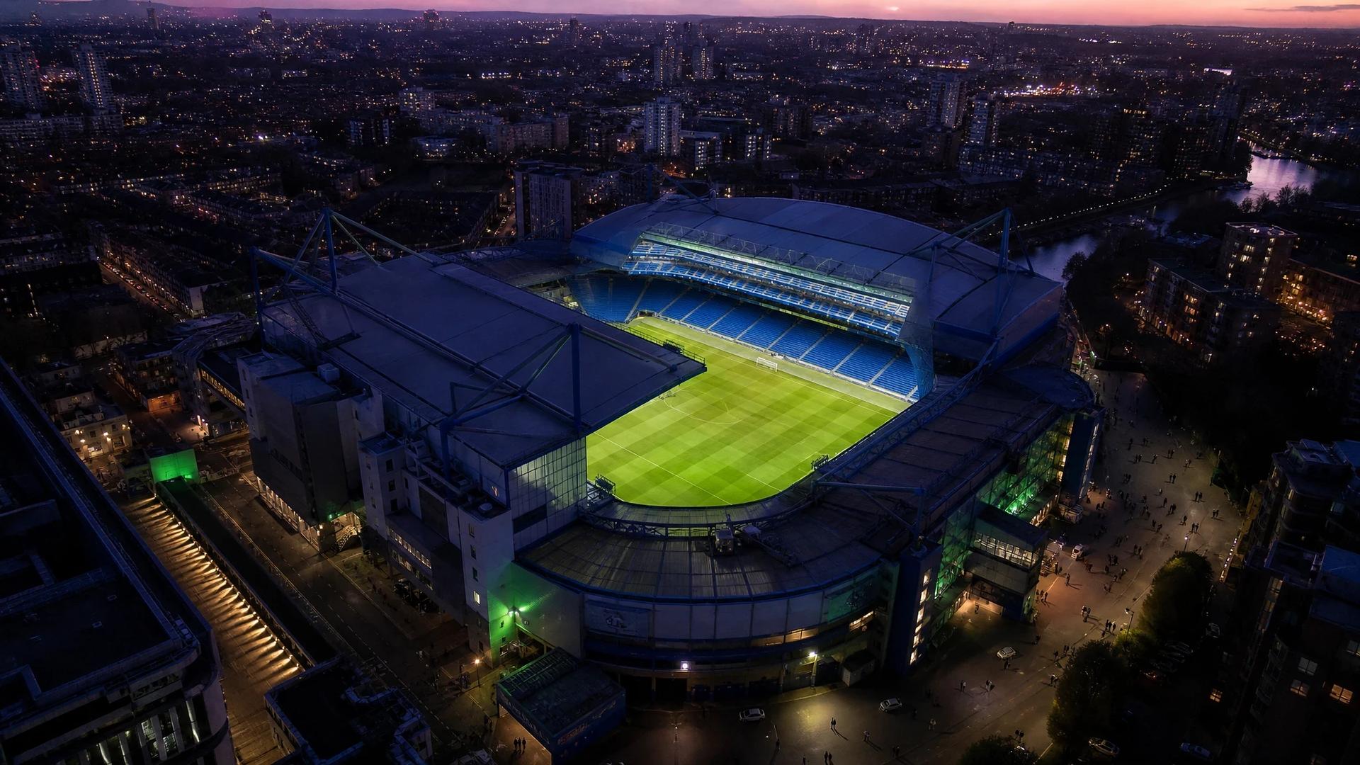 A top-down view of Stamford Bridge at dusk, with soft pastel tones and a hint of neon green lighting accent.