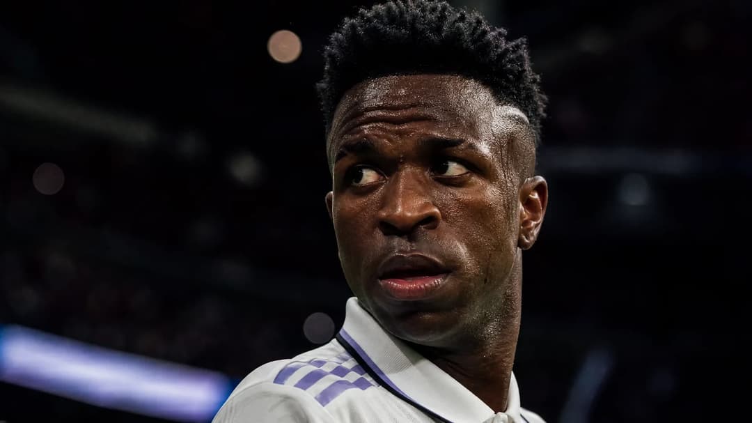Vinícius Junior in an intense close-up during a football match, lit by dramatic neon lights.