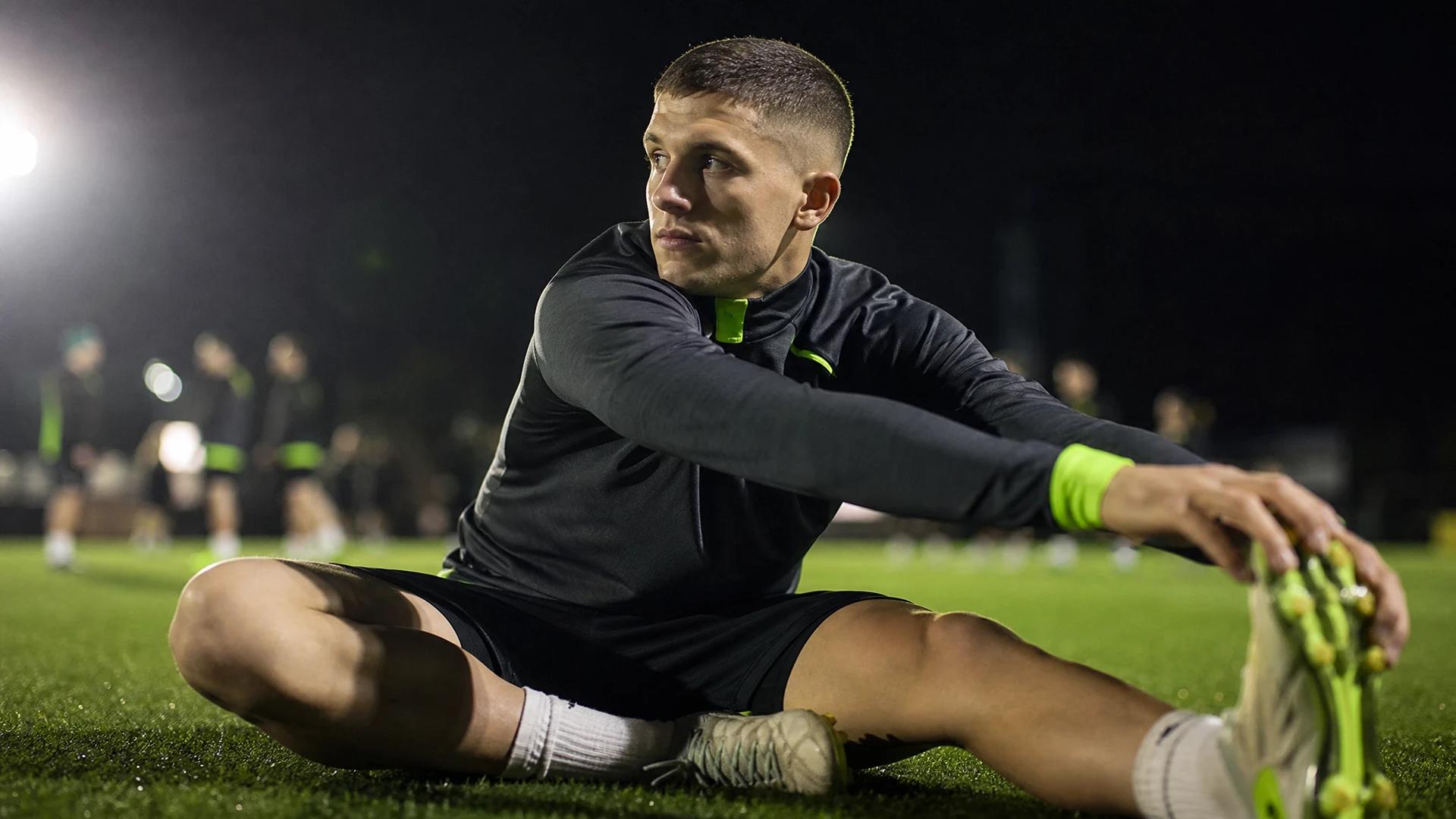 A candid moment of Christos Tzolis stretching on the Arsenal training ground, focused and determined.