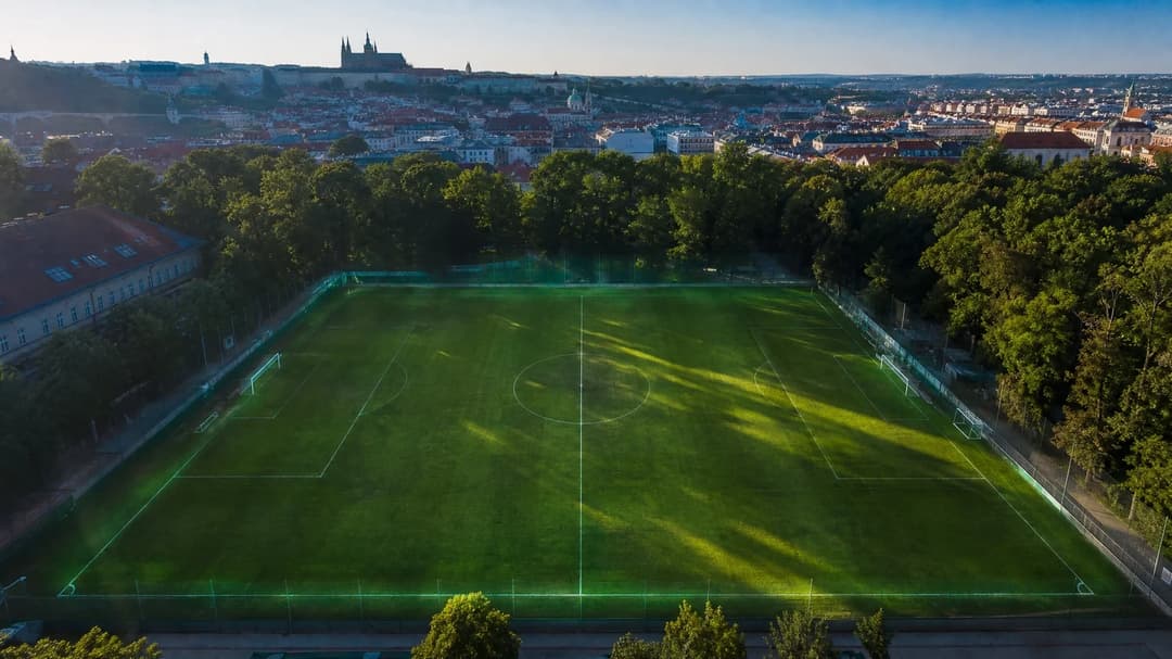 A bird's-eye view of a football pitch in Prague post-match, with dappled sunlight and a serene atmosphere.