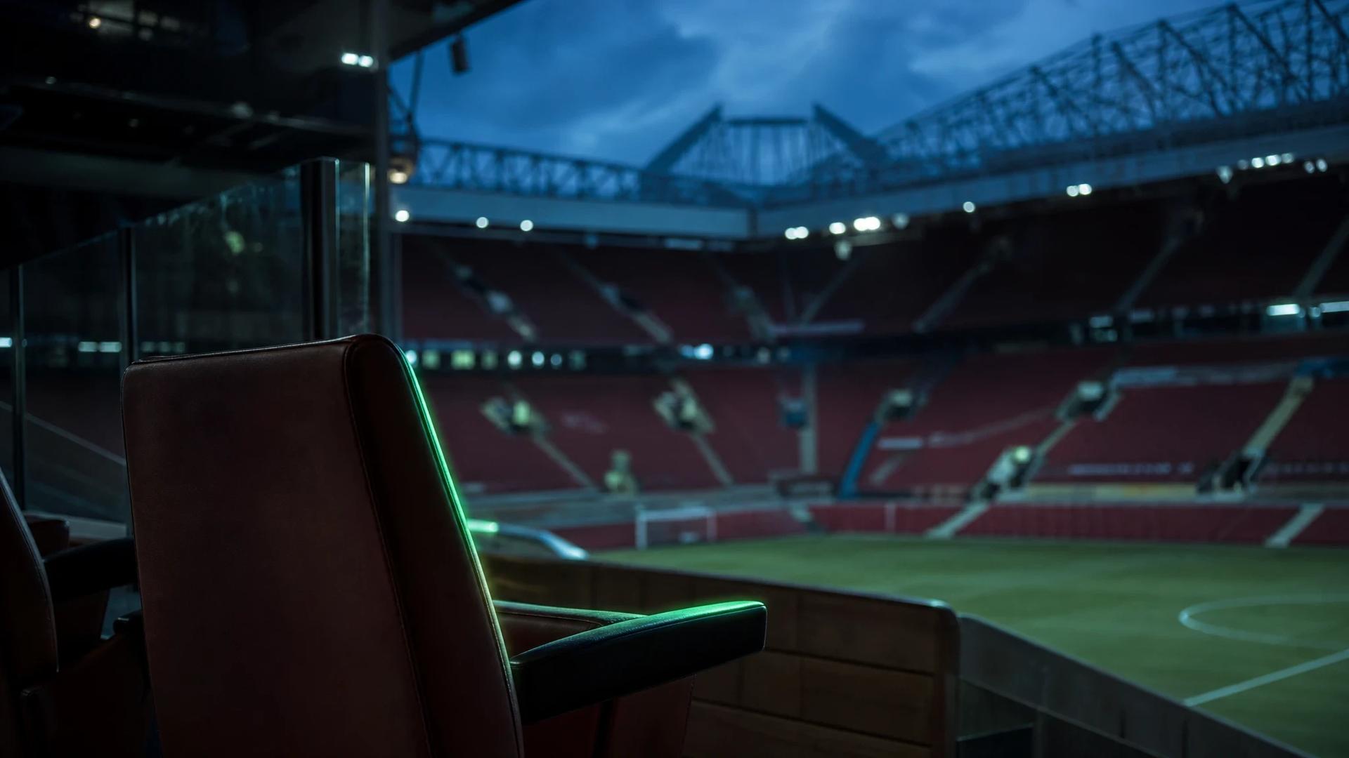 An empty seat at Old Trafford illuminated by soft light, symbolizing the tension among fans.