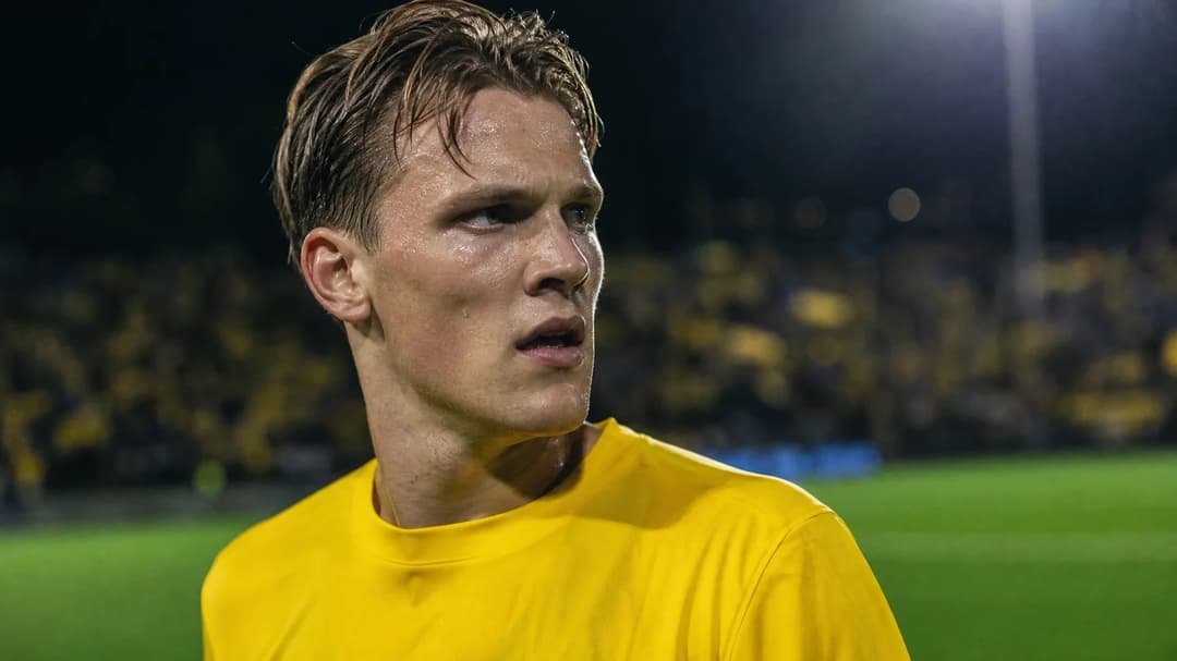Odin Bjørtuft focused on the pitch after scoring a goal, illuminated by stadium lights.