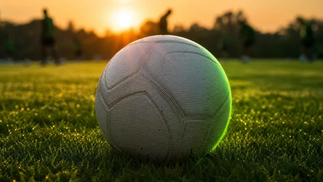 A close-up of a solitary football resting on the grass, illuminated by golden-hour backlight.
