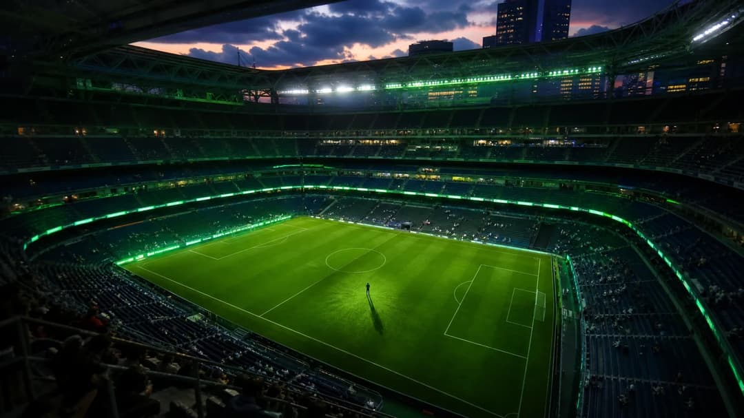 Aerial view of Santiago Bernabéu Stadium at dusk with a small figure of a young footballer on the pitch.