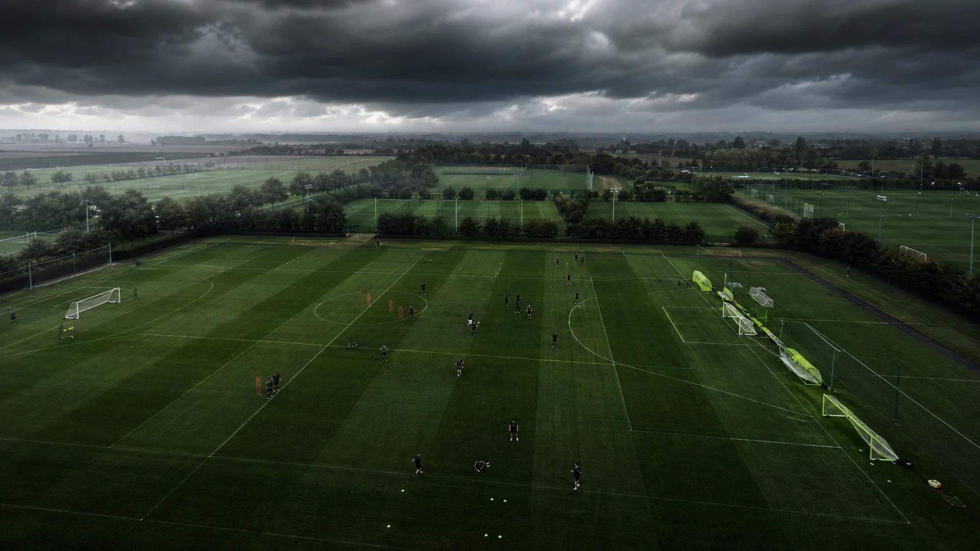Aerial view of a football training ground with players and storm clouds.