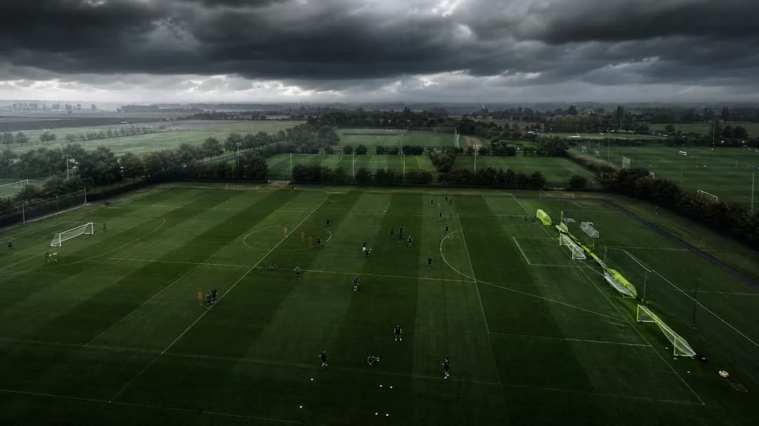 Aerial view of a football training ground with players and storm clouds.