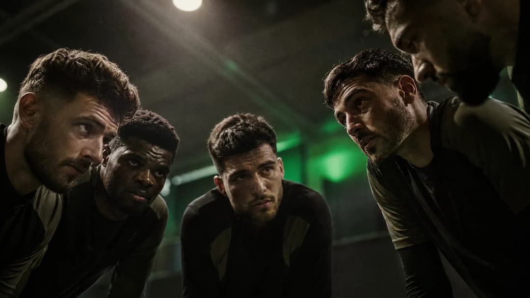 A group of Arsenal players in a meeting, faces revealing determination under dramatic lighting.