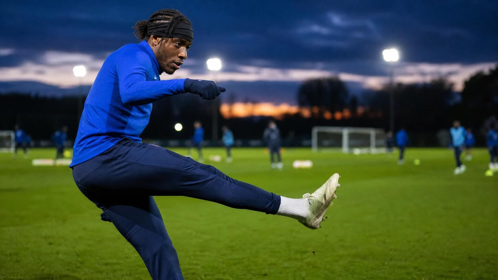 Noni Madueke executing a kick during a training session at dusk.