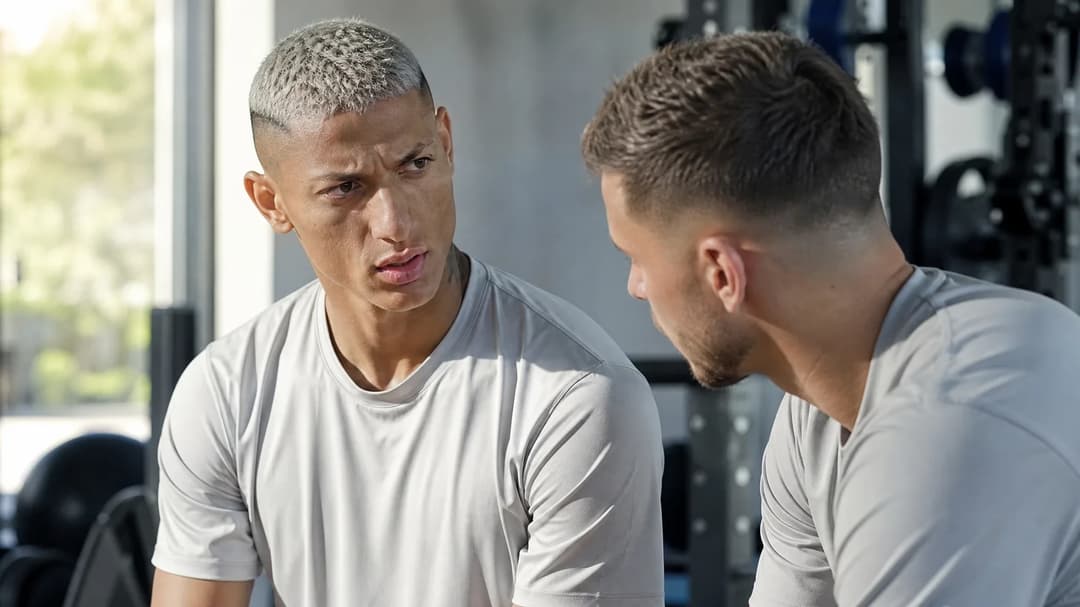 Richarlison and a teammate engaged in a serious conversation in a training room.