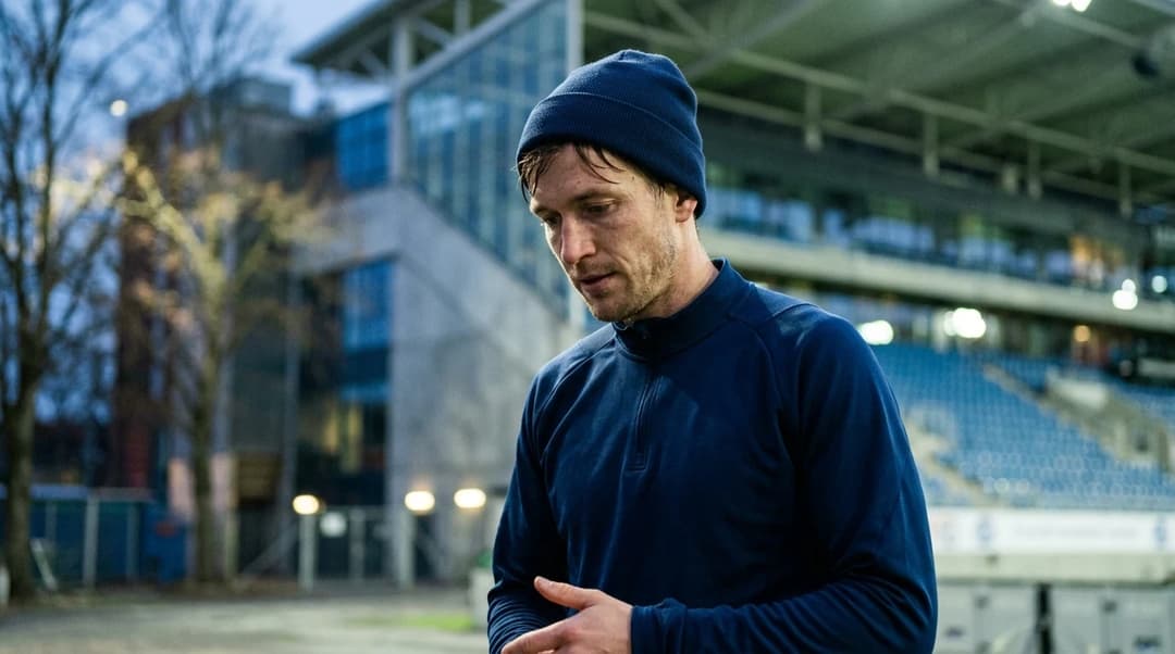 A football player from Vålerenga reflecting after a match, illuminated by dappled light in the background.
