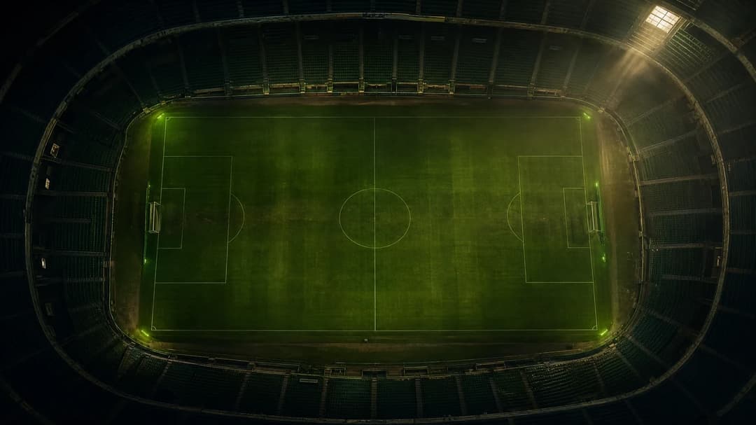 A bird's-eye view of a football pitch with subtle green highlights, capturing a moment of stillness.