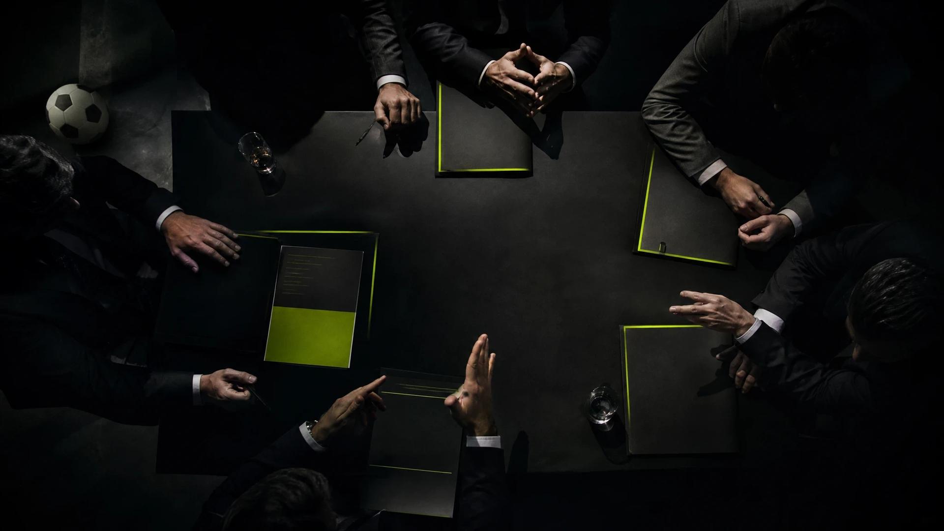 A top-down view of a dark conference room with figures negotiating over documents about Harry Kane's contract.