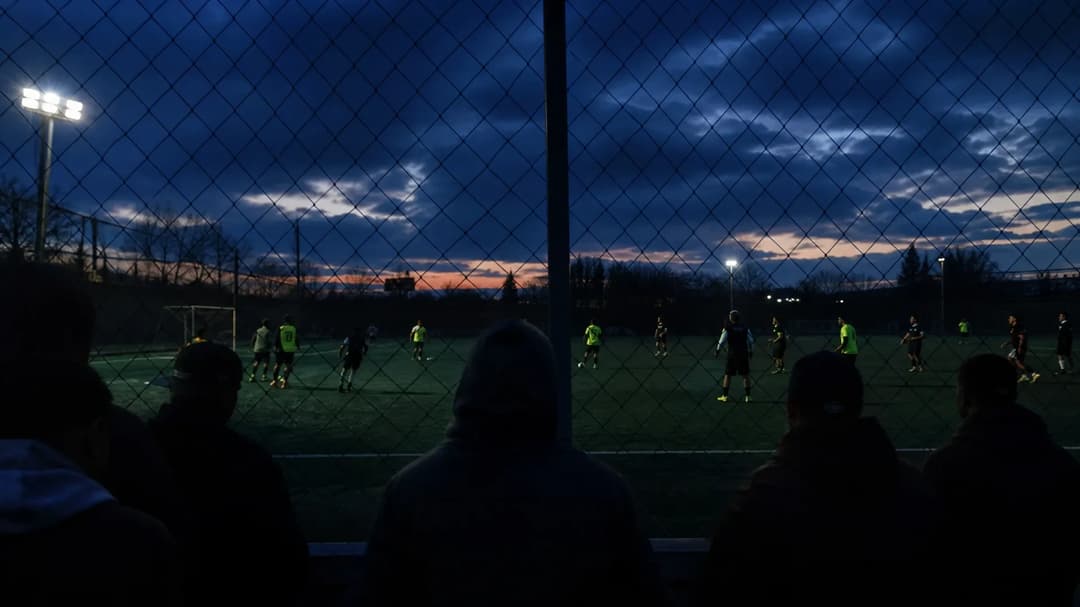 A night scene of Manchester United players training under dim lighting, with shadows of spectators in the foreground.
