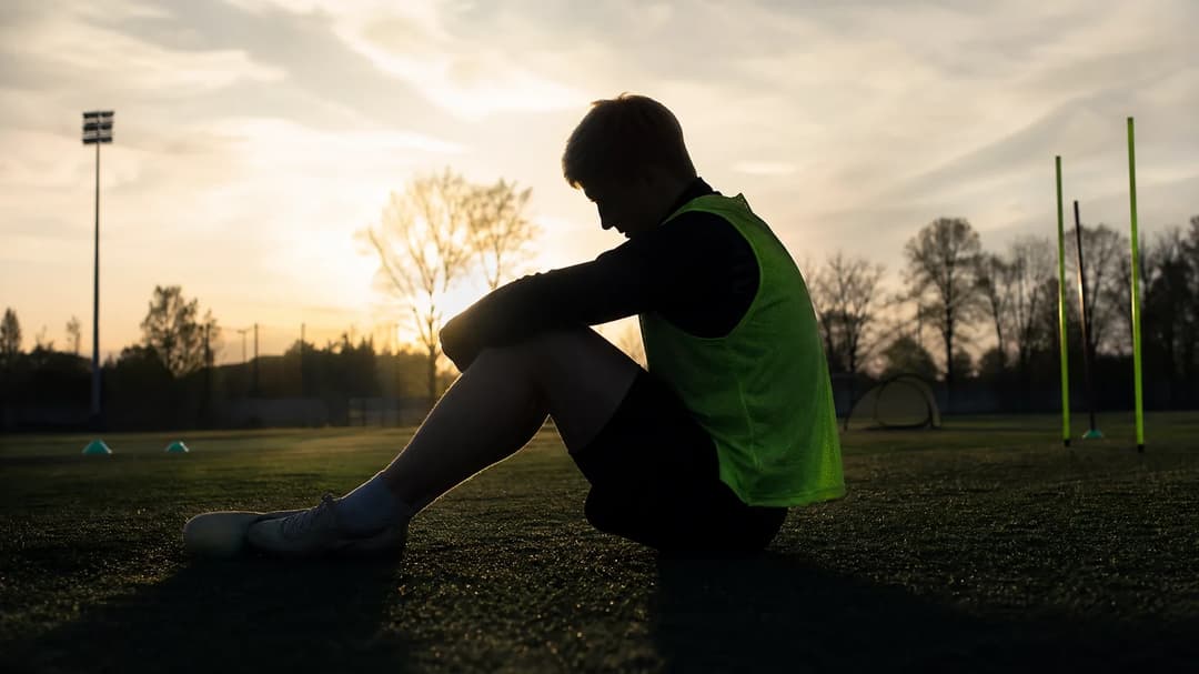 A silhouette of a football player is set against a bright training ground background, evoking a sense of tension and reflection.