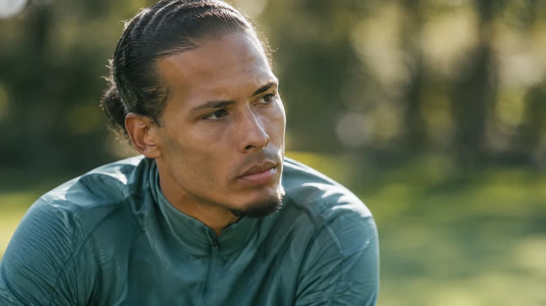 Virgil van Dijk in a candid moment during a football training session with dappled sunlight filtering through trees.