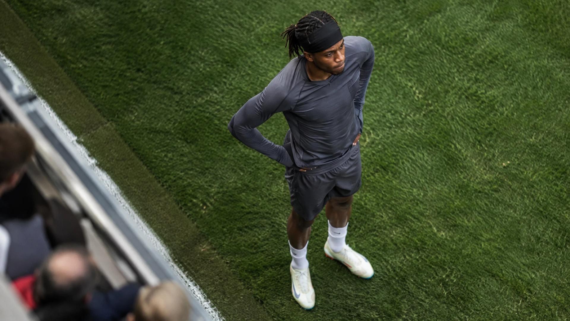 Noni Madueke warming up on the pitch with a focused expression.