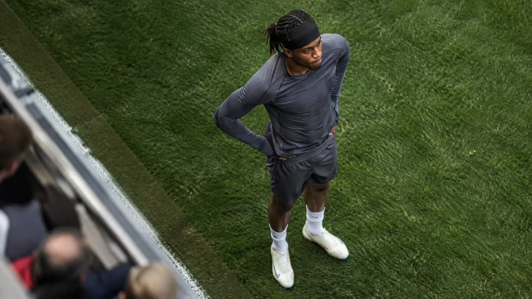 Noni Madueke warming up on the pitch with a focused expression.